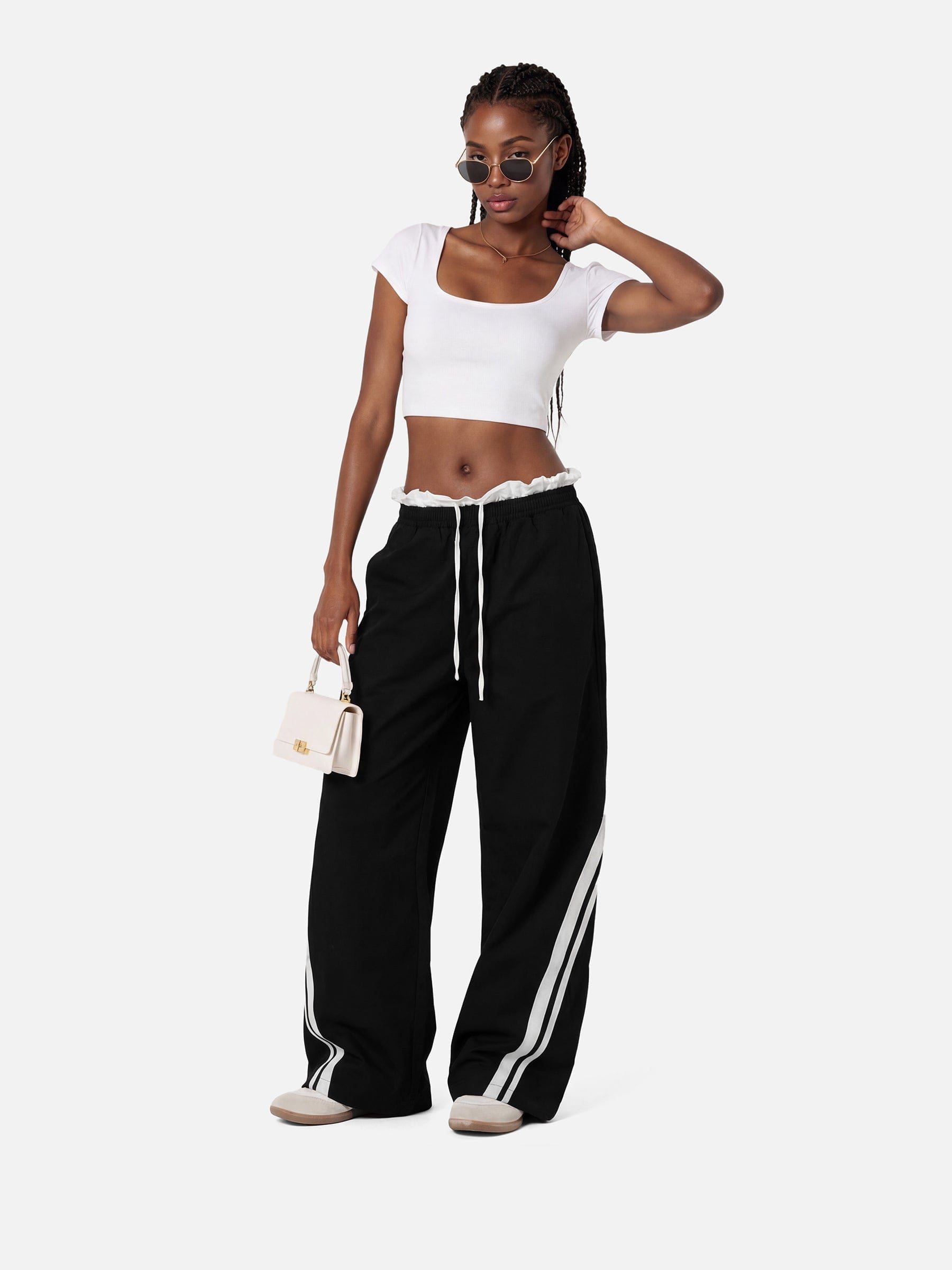 Woman wearing a white crop top and black pants with white stripes on a white background