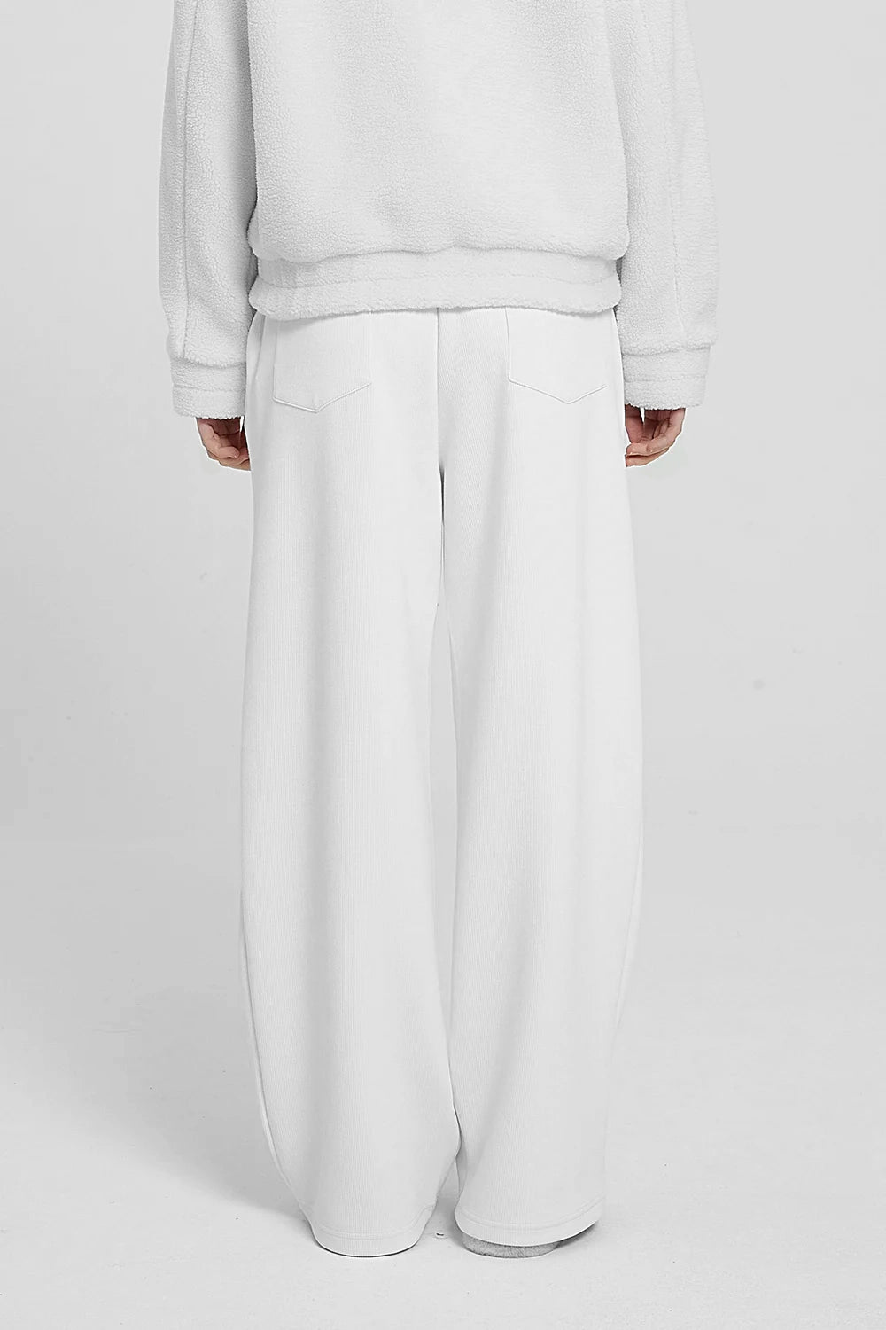 white high waist knitted pants and a white hoodie with a logo on the sleeve