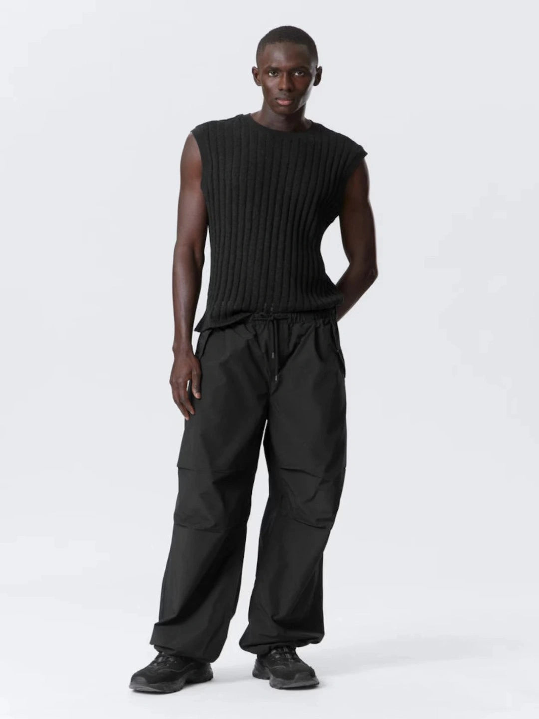 Person wearing a black sleeveless top and black pants on a white background
