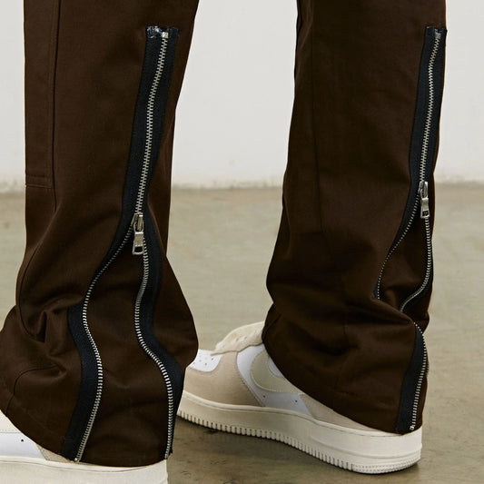Brown pants with zippers on the sides worn with beige sneakers on a neutral background