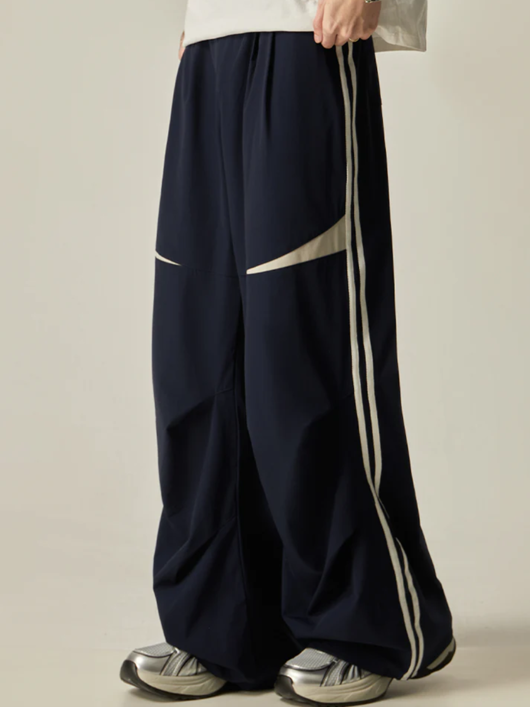 A person standing sideways, wearing a white t-shirt and navy parachute pants with white side stripes, paired with white sneakers.