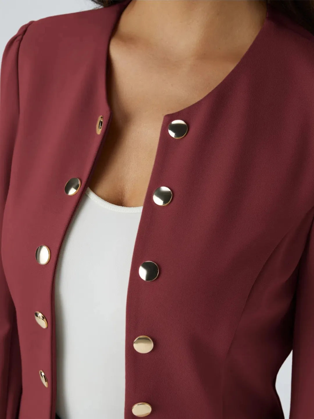Woman wearing a maroon buisness jacket with gold buttons on a light gray background