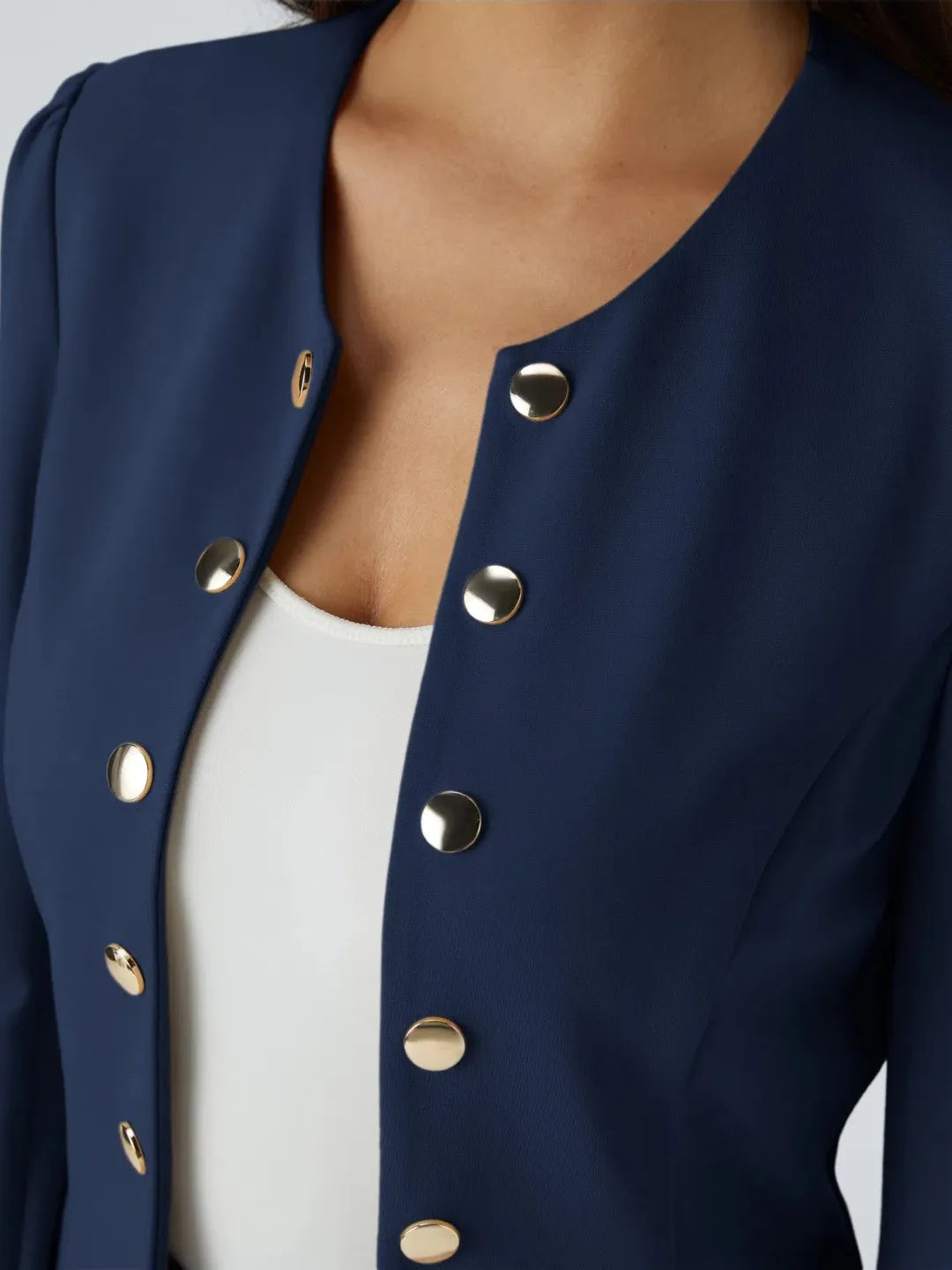 Woman wearing a blue buisness jacket with gold buttons on a light gray background