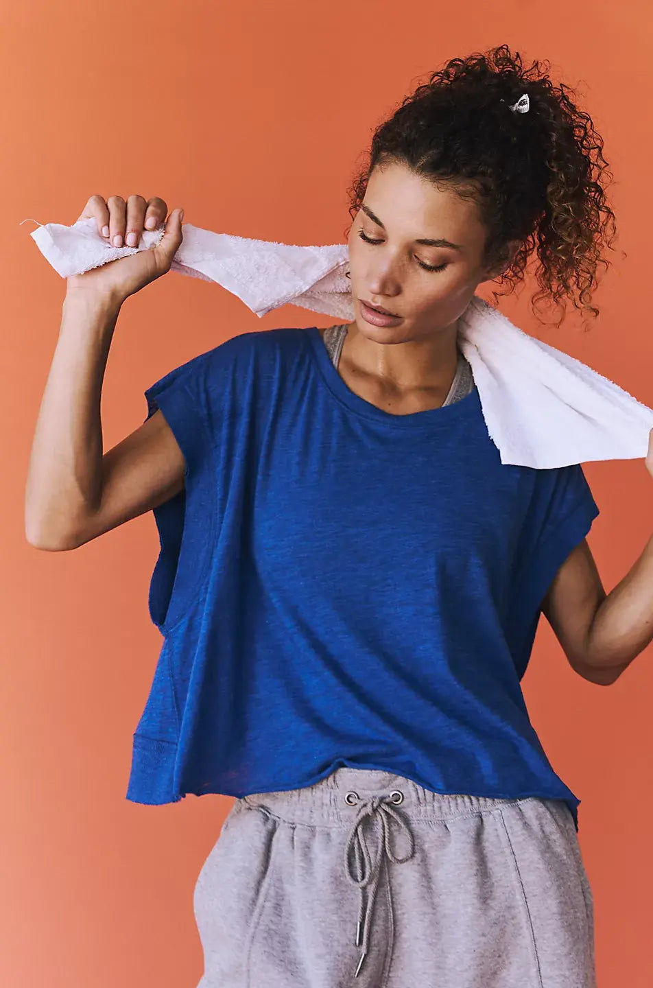 Woman in blue shirt and gray pants holding a white towel over her shoulder against an orange background