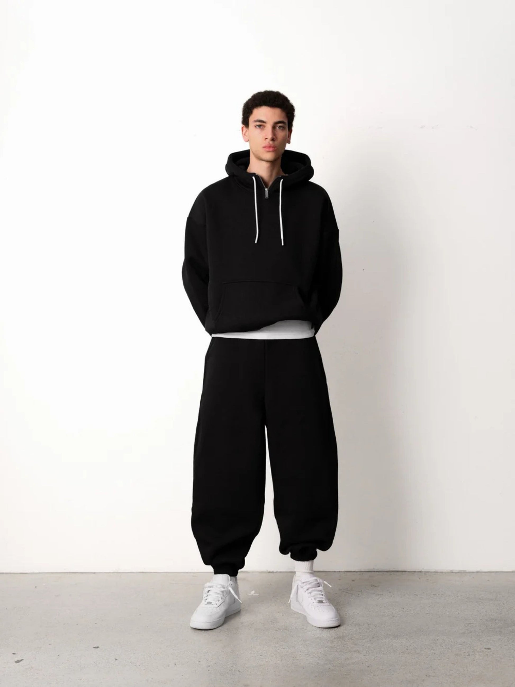 Person wearing a black hoodie and black pants with white shoes on a white background
