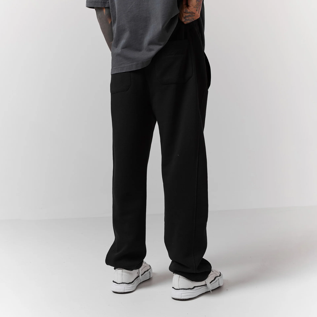 Person wearing black pants and white sneakers on a plain background