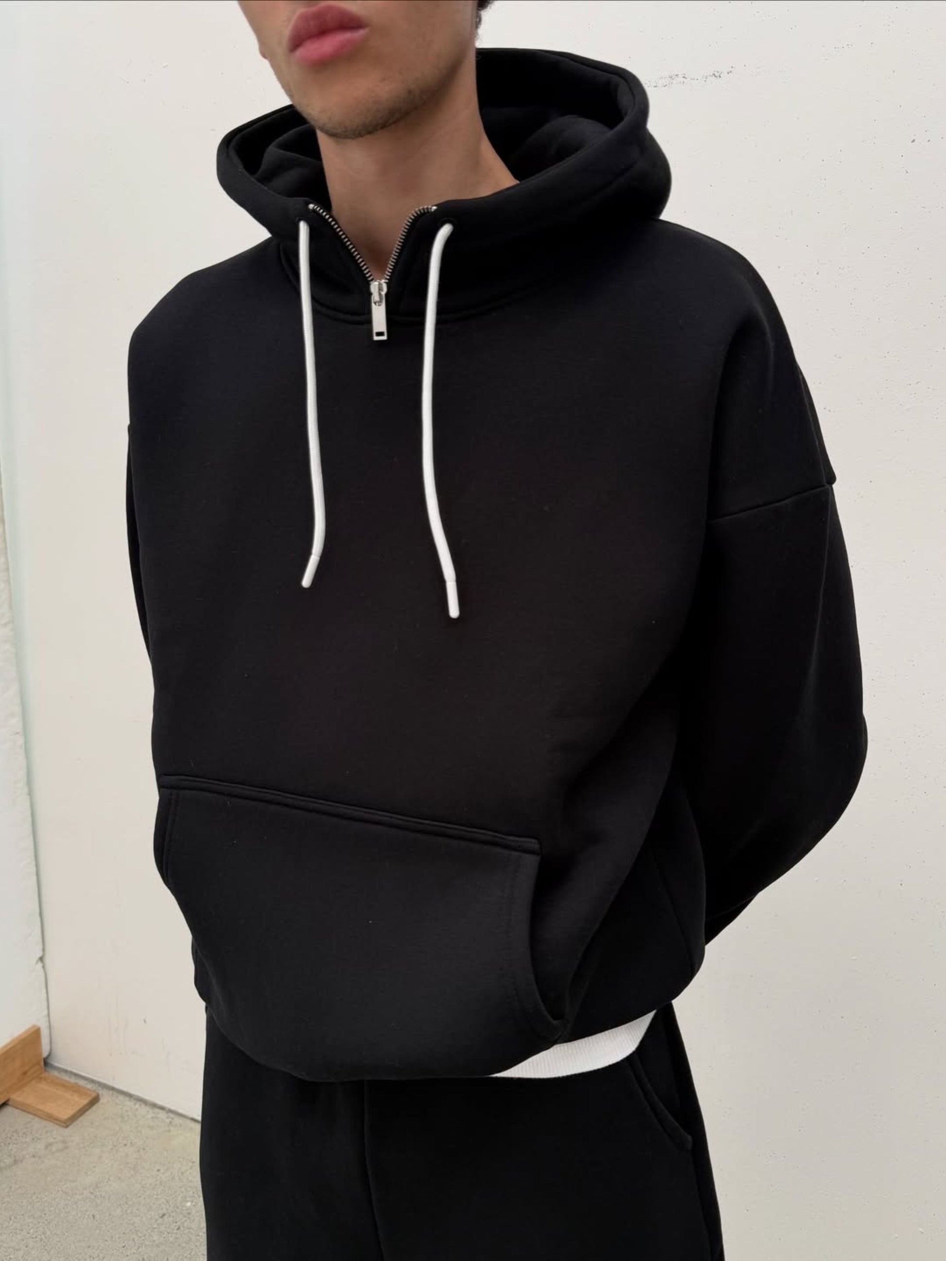 Person wearing a black hoodie with white drawstrings against a plain background