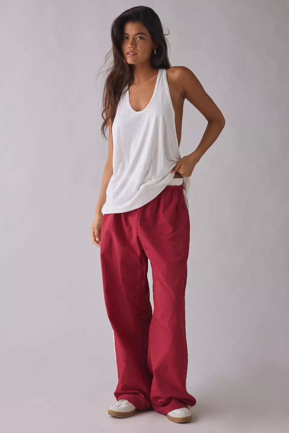 Woman wearing a white tank top and red pants on a plain background