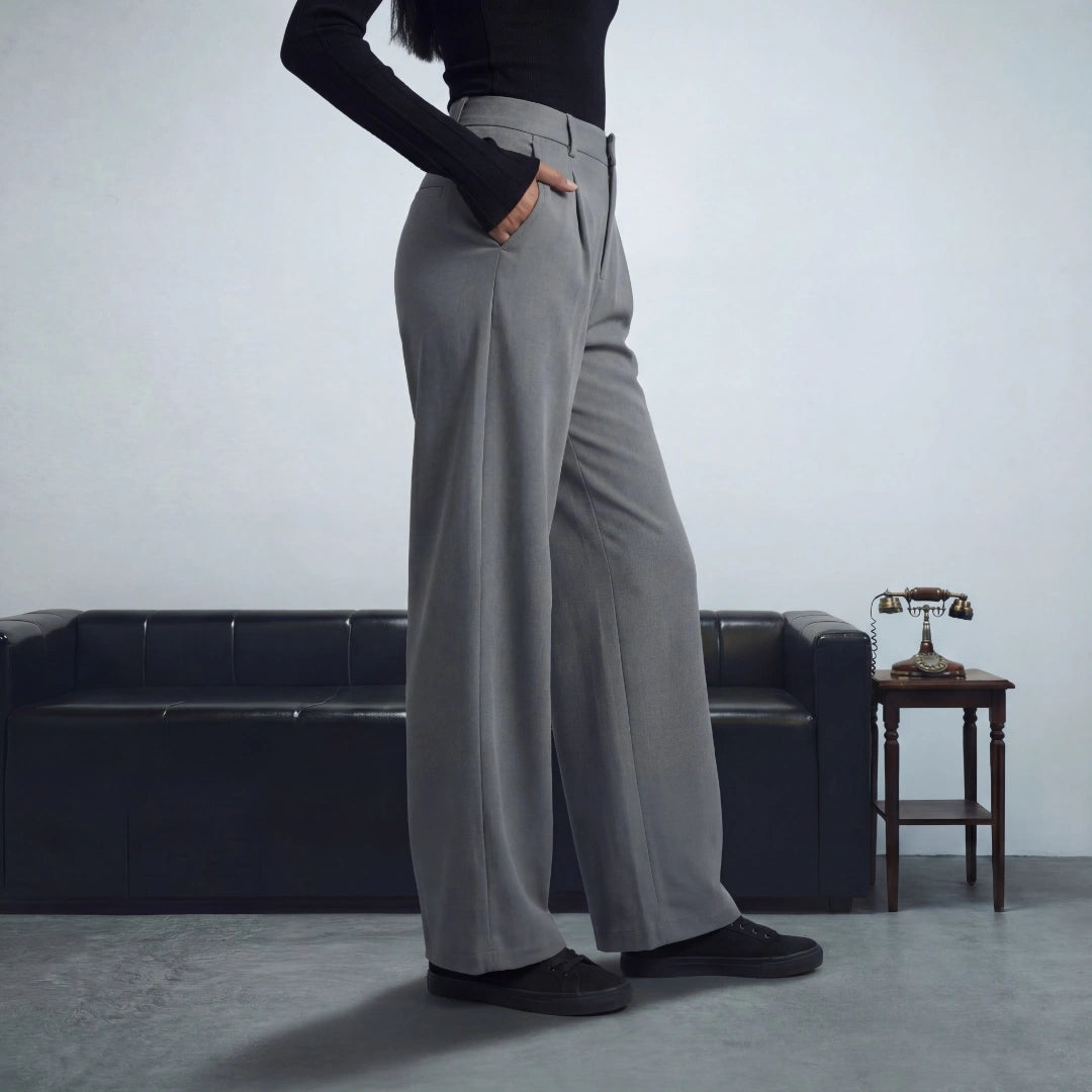 Person wearing gray wide-leg pants in a minimalistic room with a sofa and small table.