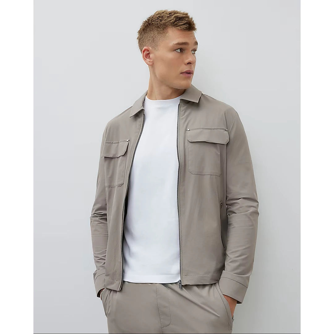 Man wearing a beige jacket over a white shirt on a light gray background