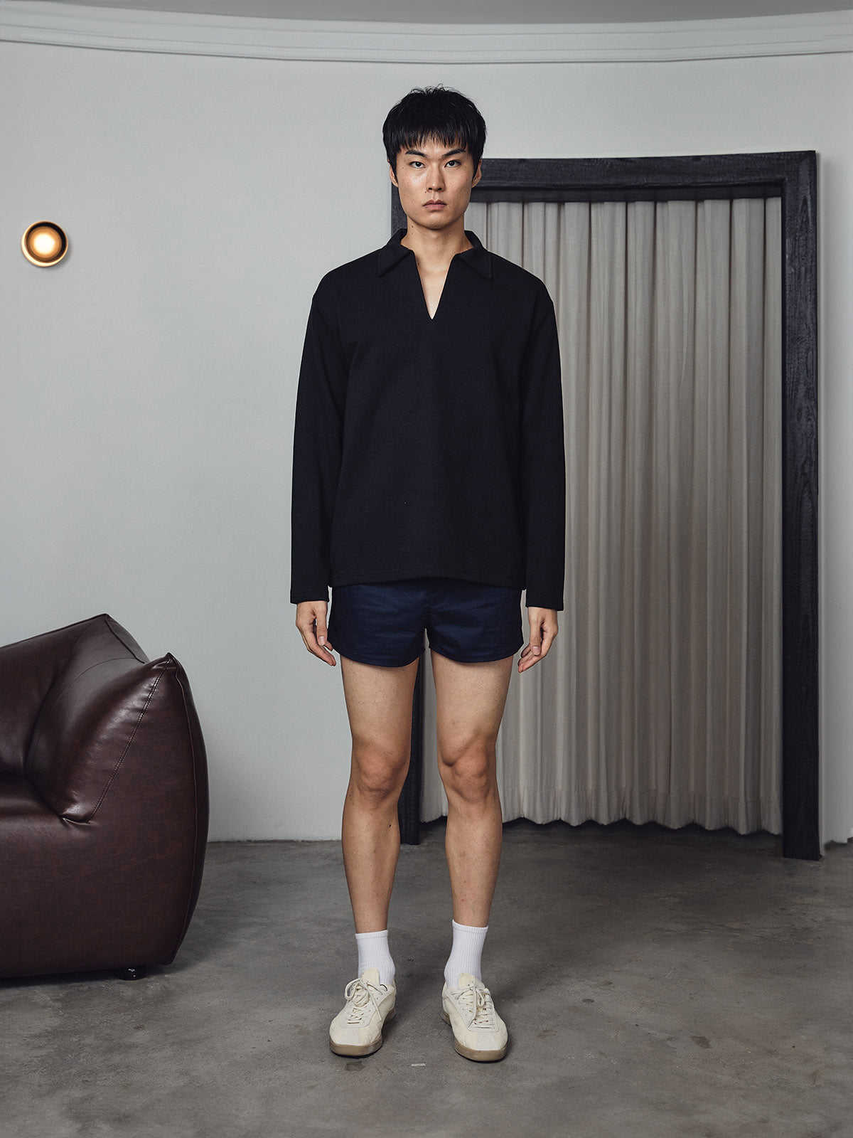 Man wearing a black shirt and dark shorts standing in a minimalistic room.
