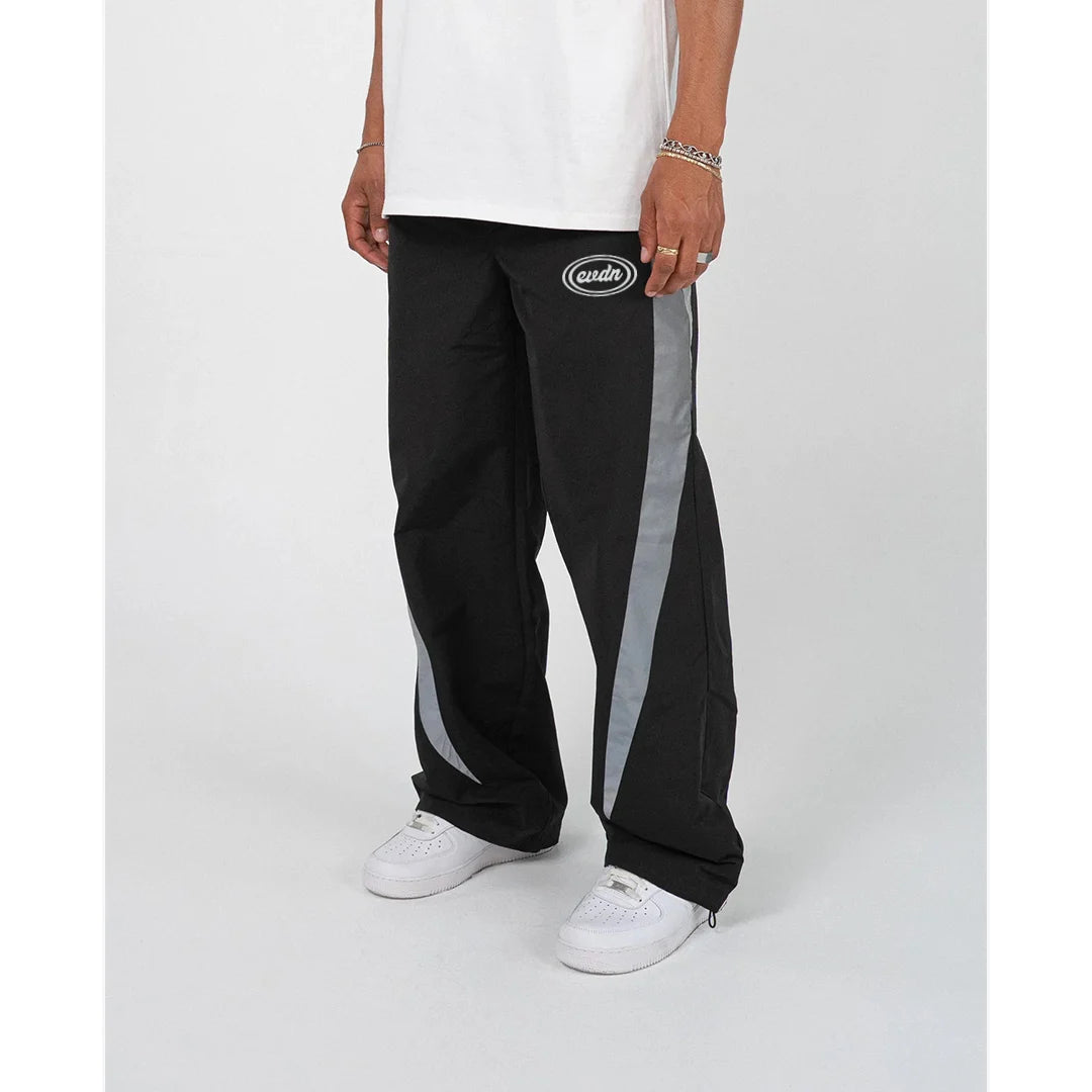 Person wearing black track pants with a logo on a white background