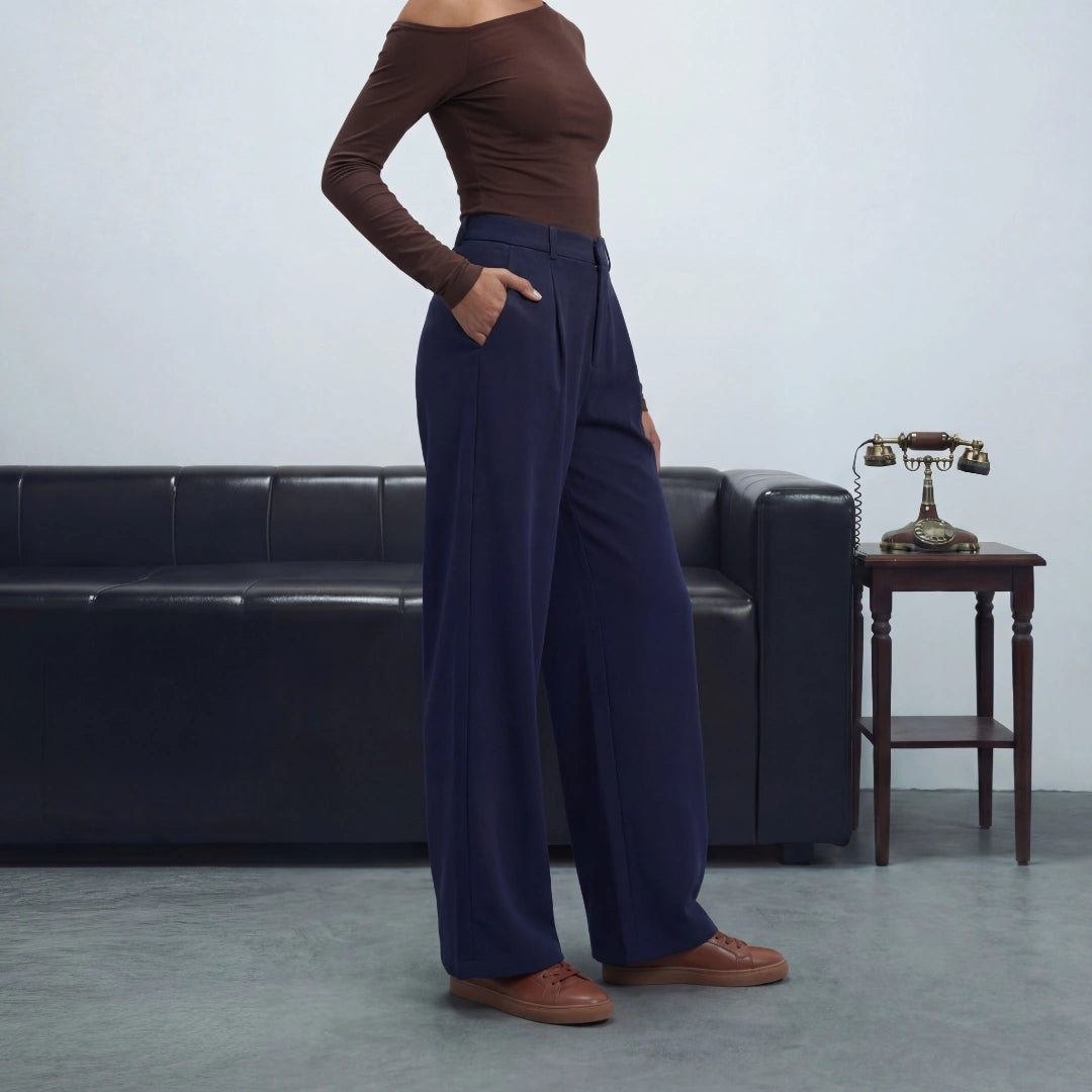 Person wearing a brown top and navy pants standing in a room with a black leather couch and wooden table.