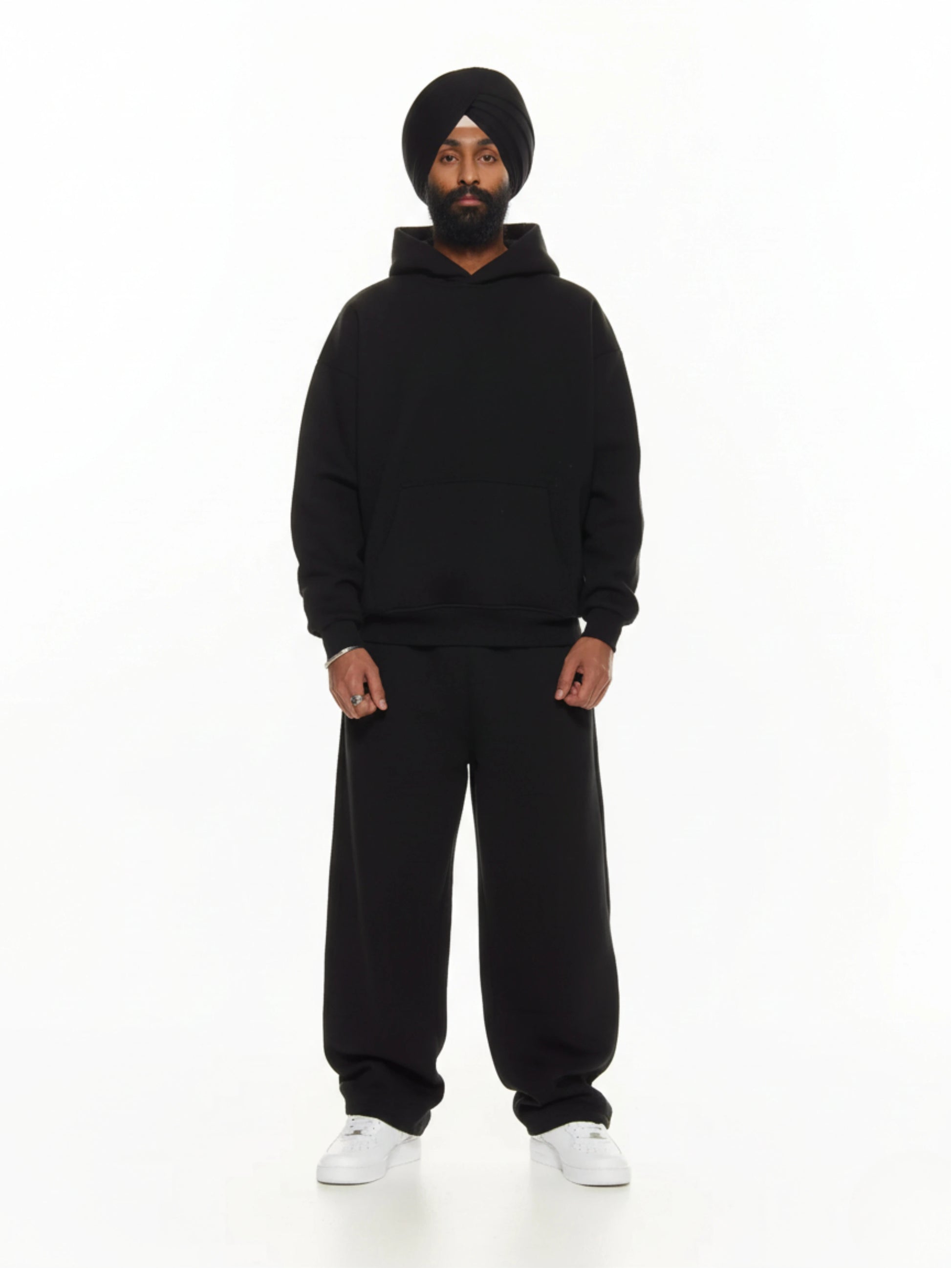 Person wearing a black hoodie and pants with a black turban on a white background