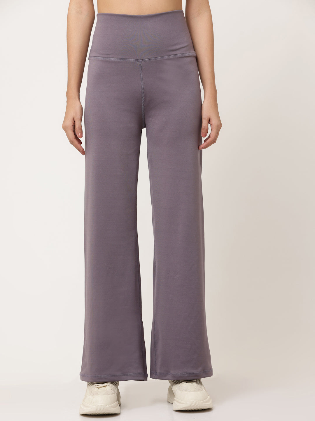 A woman standing and posing in lavender high-waisted full-length yoga pants with a solid black sports top.