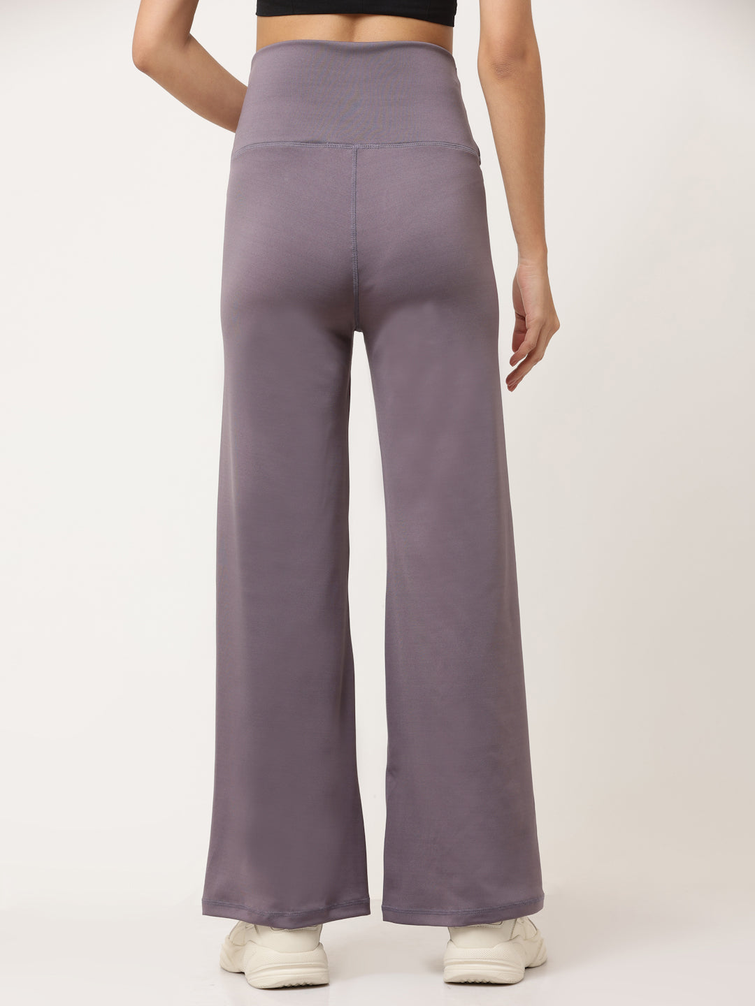 A woman standing and posing in lavender high-waisted full-length yoga pants with a solid black sports top.