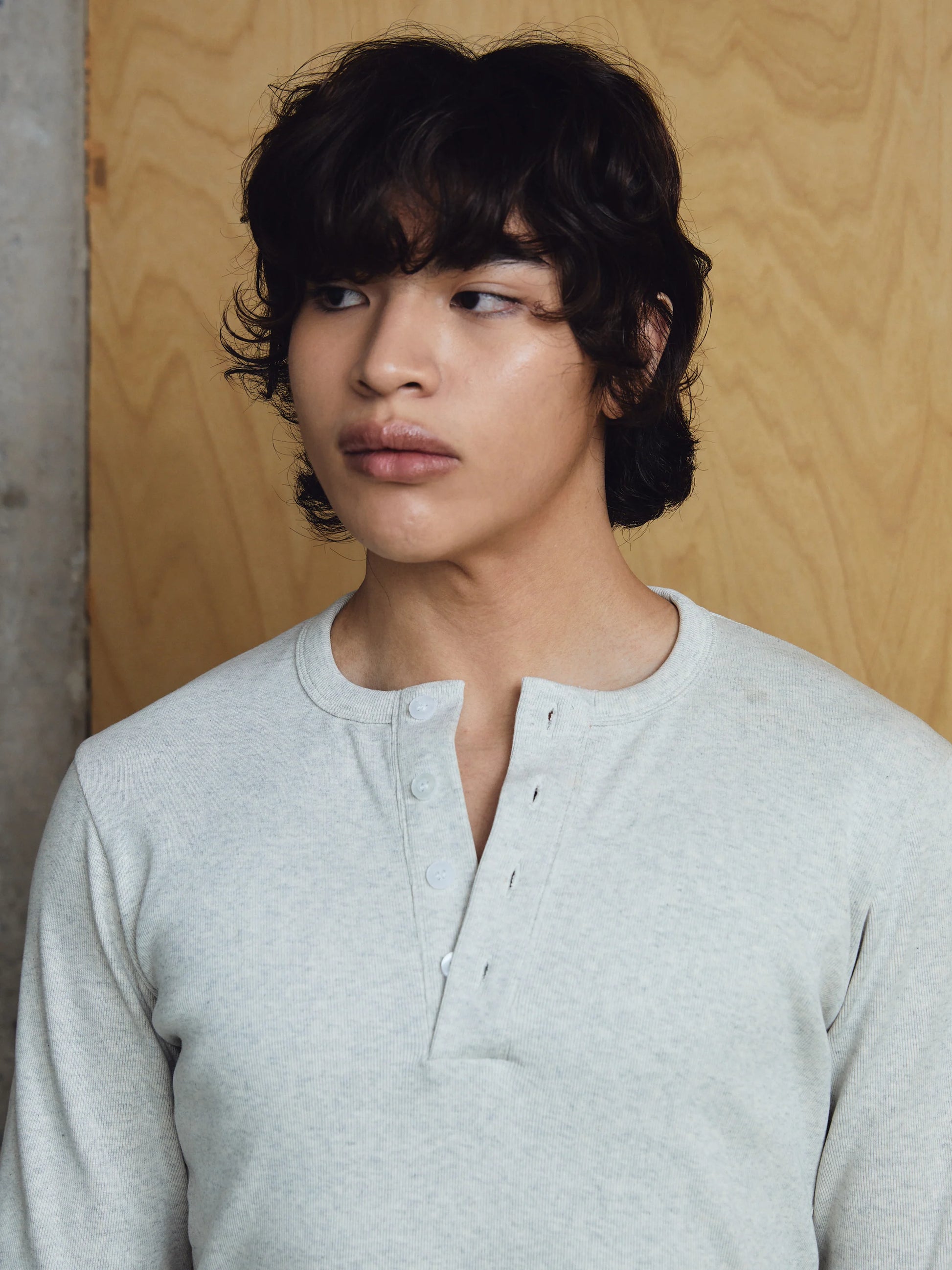 Person wearing a light grey henley shirt against a wooden background