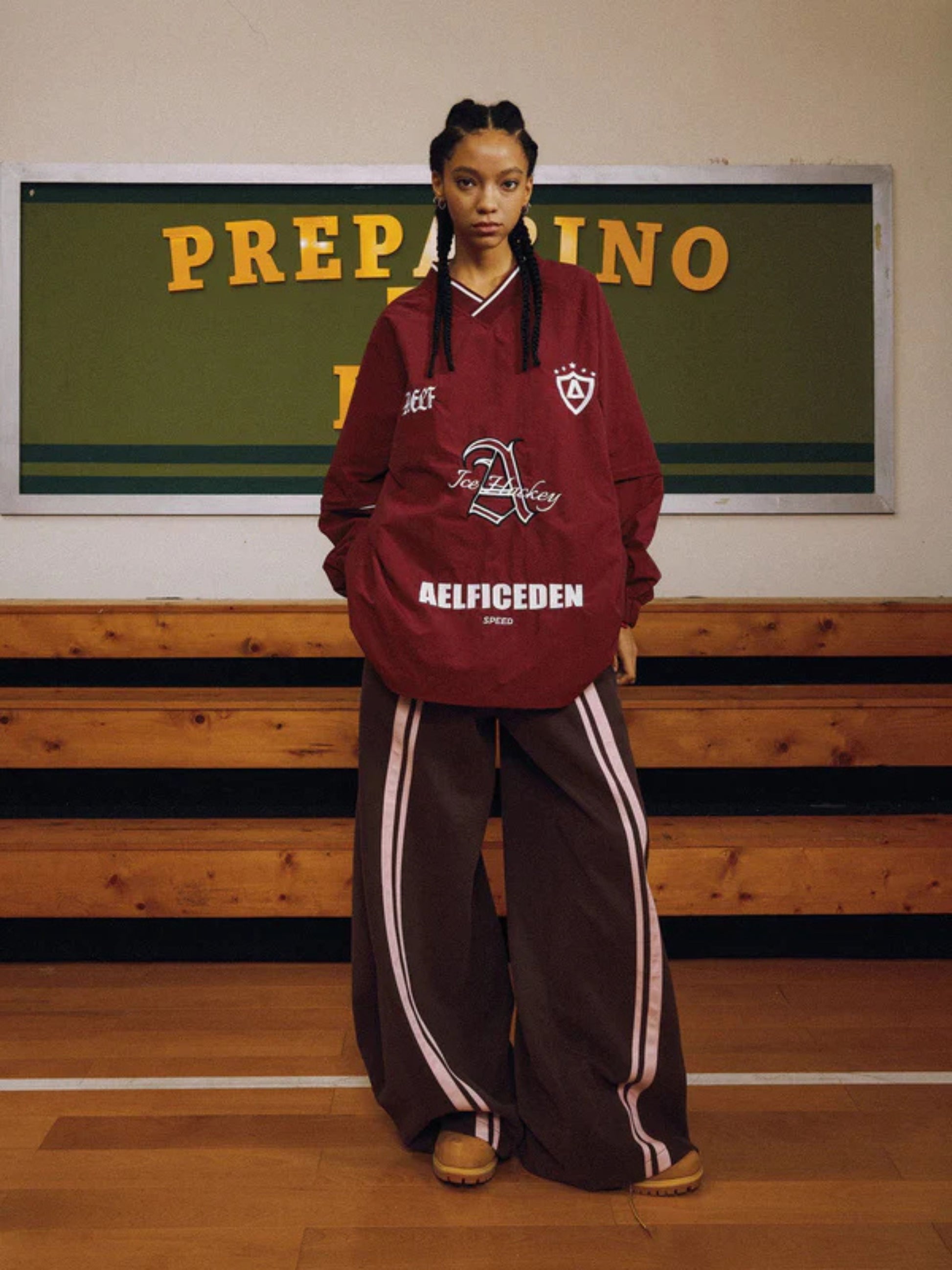 Person wearing a maroon hoodie and brown tracksuit in a gymnasium setting