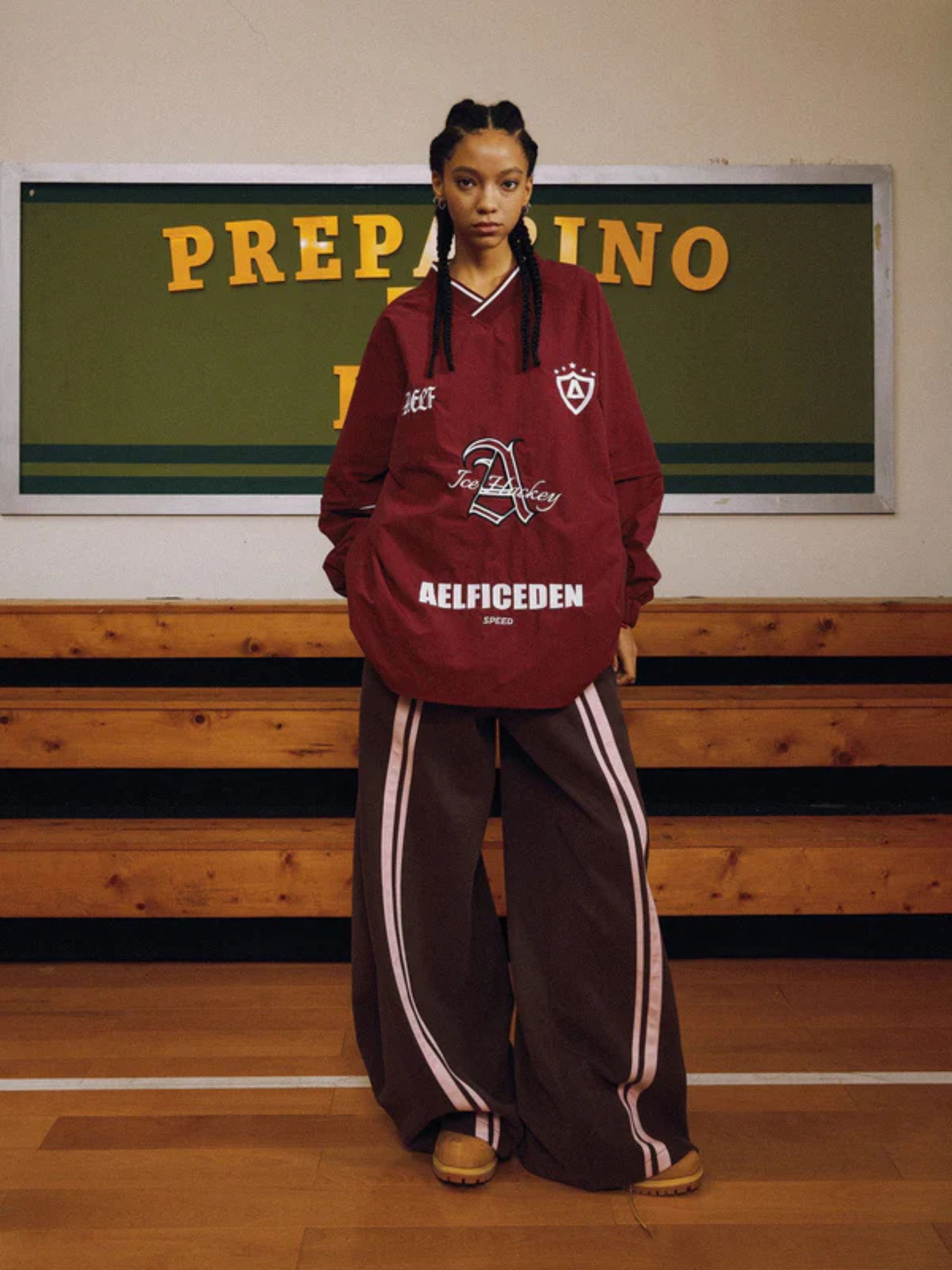 Person wearing a maroon hoodie and brown tracksuit in a gymnasium setting