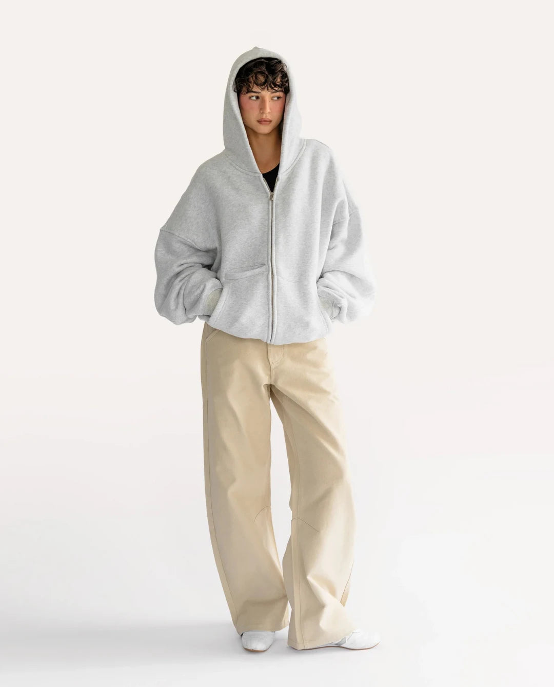 Person wearing a gray hoodie and beige pants on a white background