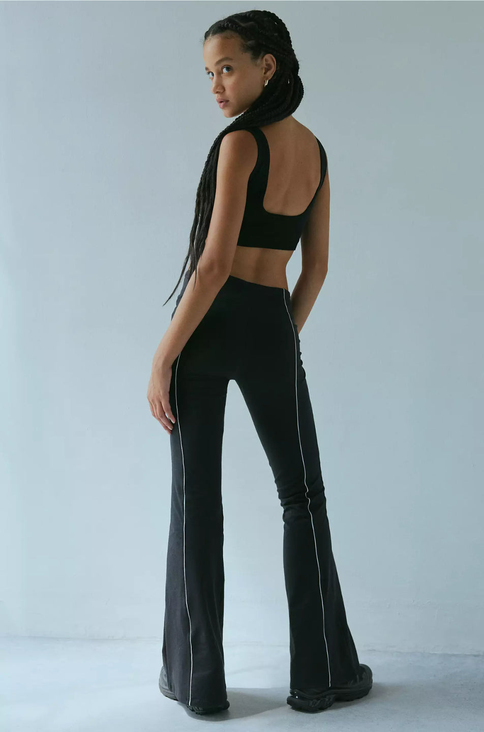 A woman modeling black piped flare pants with a wide fit and high waist.