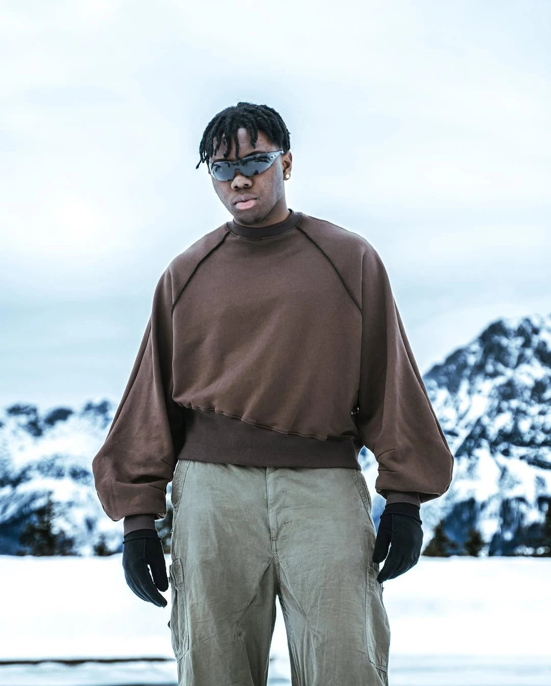 Person wearing a brown sweater and green pants standing in a snowy landscape