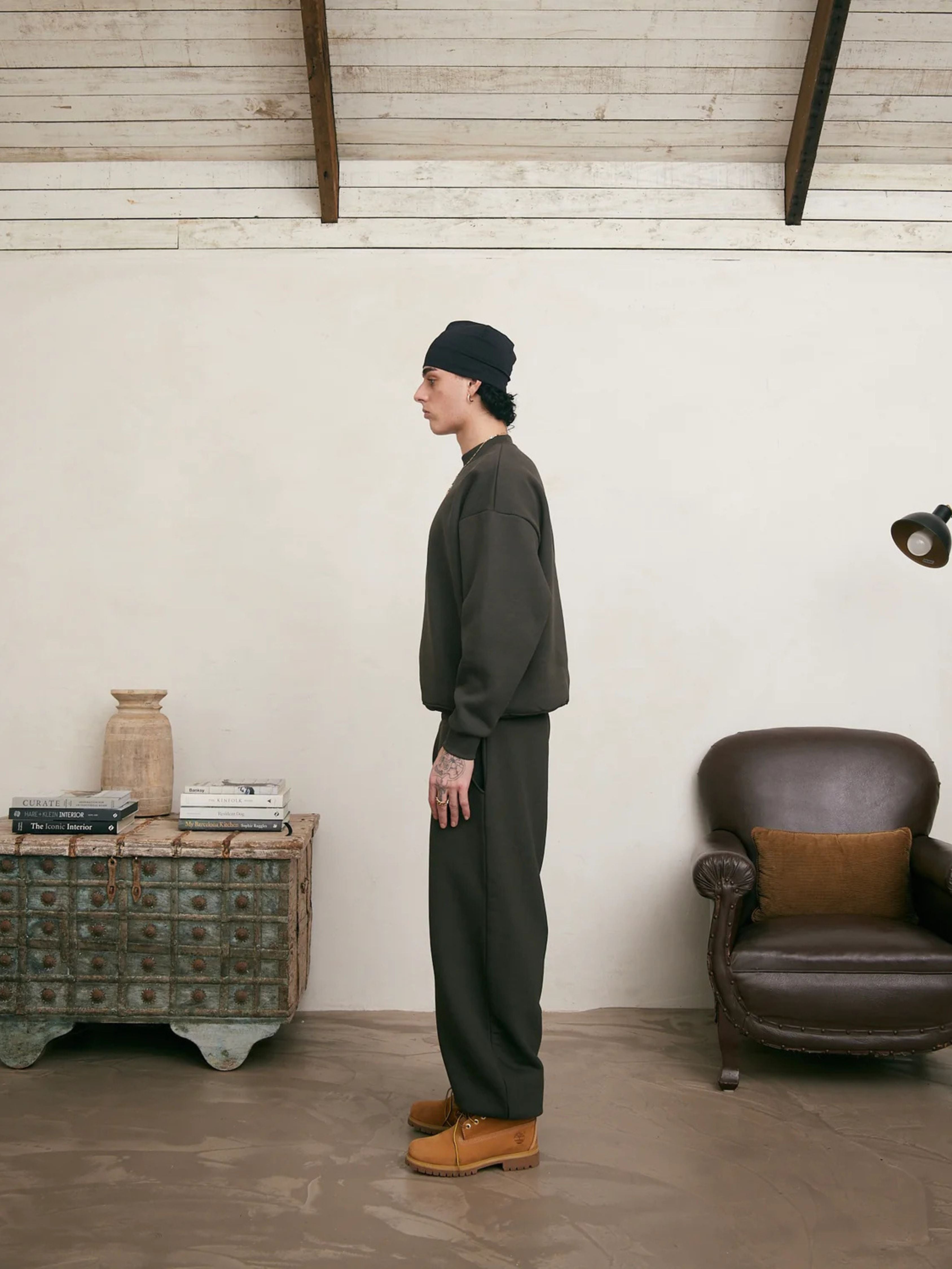 Person standing in a room with a white wall, brown chair, and wooden cabinet.