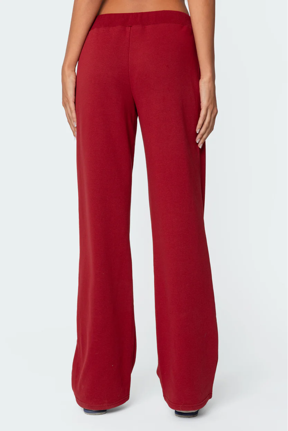 A female model wearing a white tank top and red lowrise trackpants with the number '06' printed on the left leg.