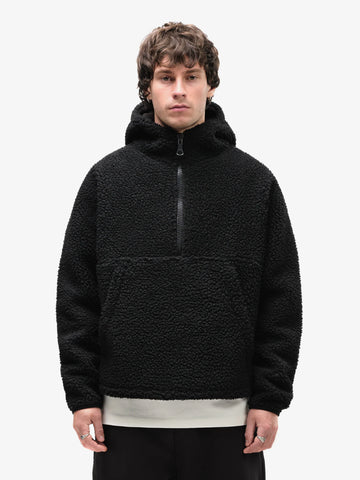 A male model wearing a black fleece half-zip hoodie with a kangaroo pocket, standing against a white background.