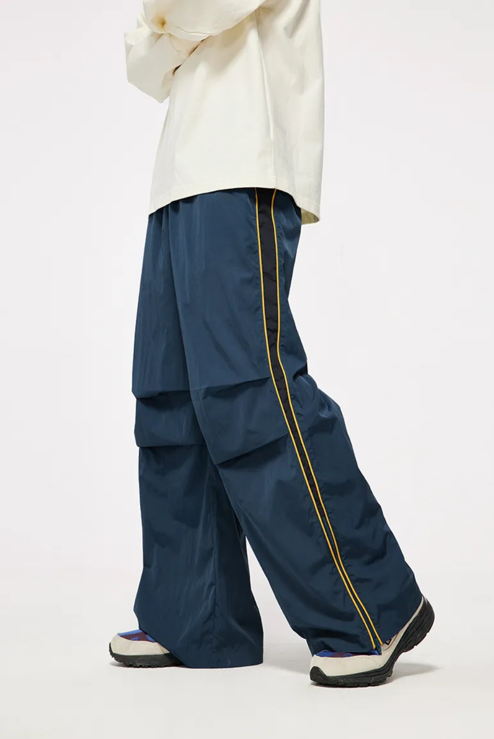 A person wearing vintage sporty pants in red-brown color, standing next to a skateboard.