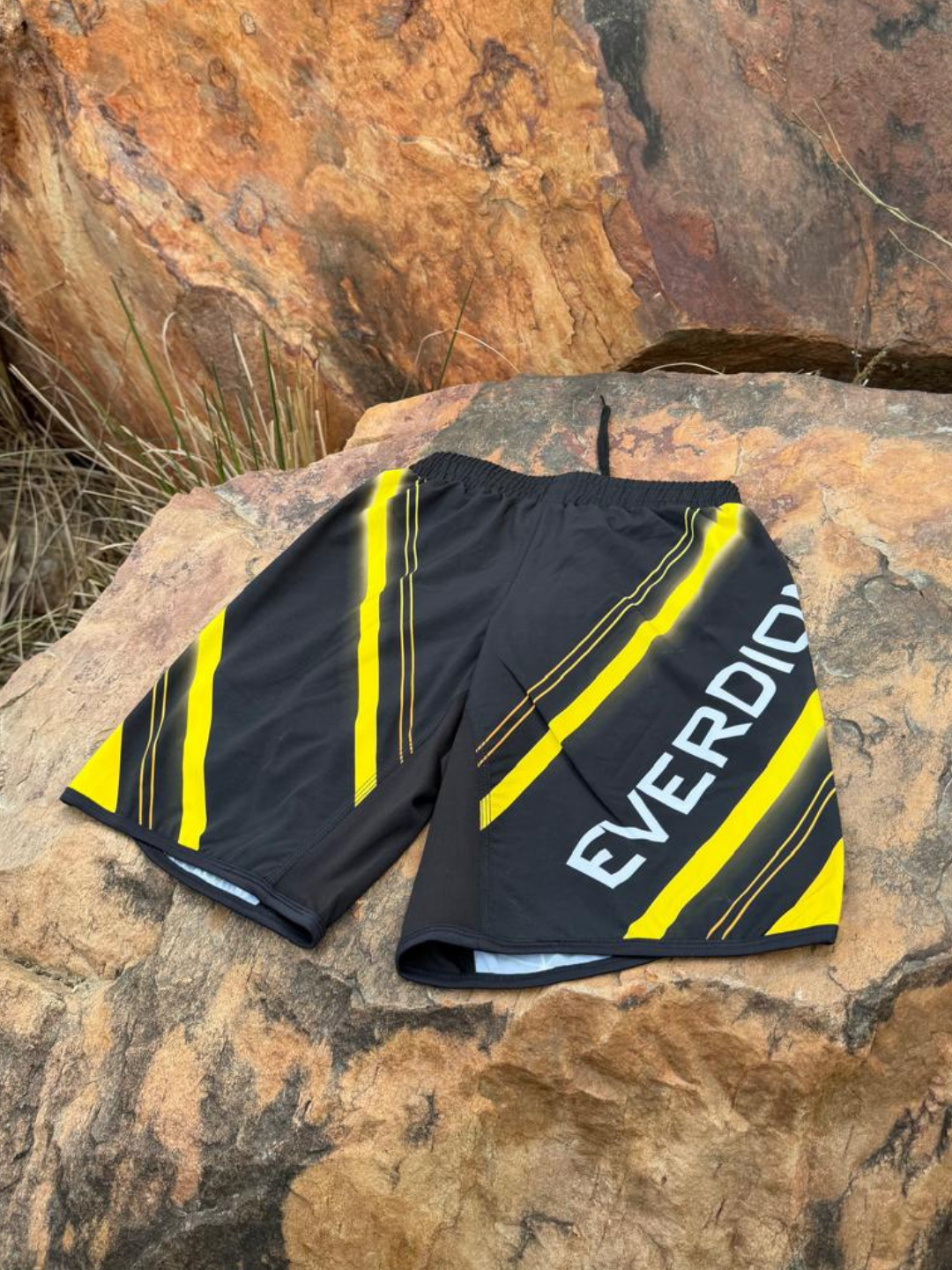 Black and yellow shorts with 'EVERDION' branding on a rocky surface