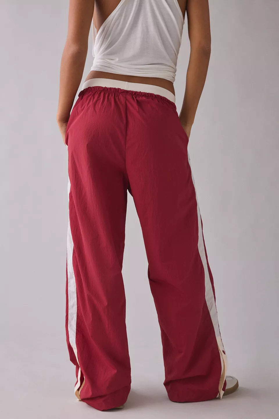 Person wearing red track pants with white stripes on a plain background