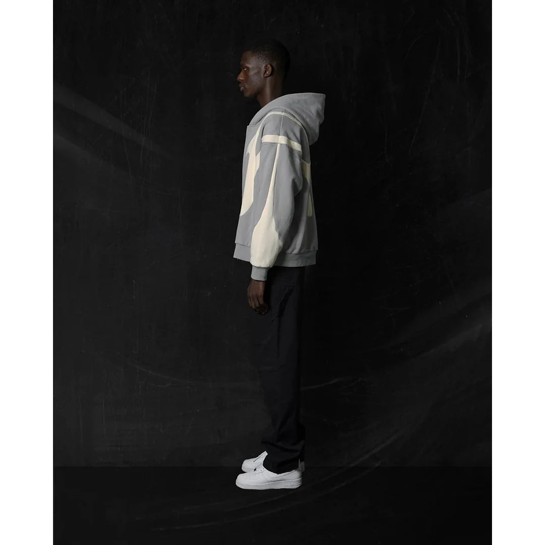 Person wearing a light gray hoodie with a geometric design, standing against a dark background.