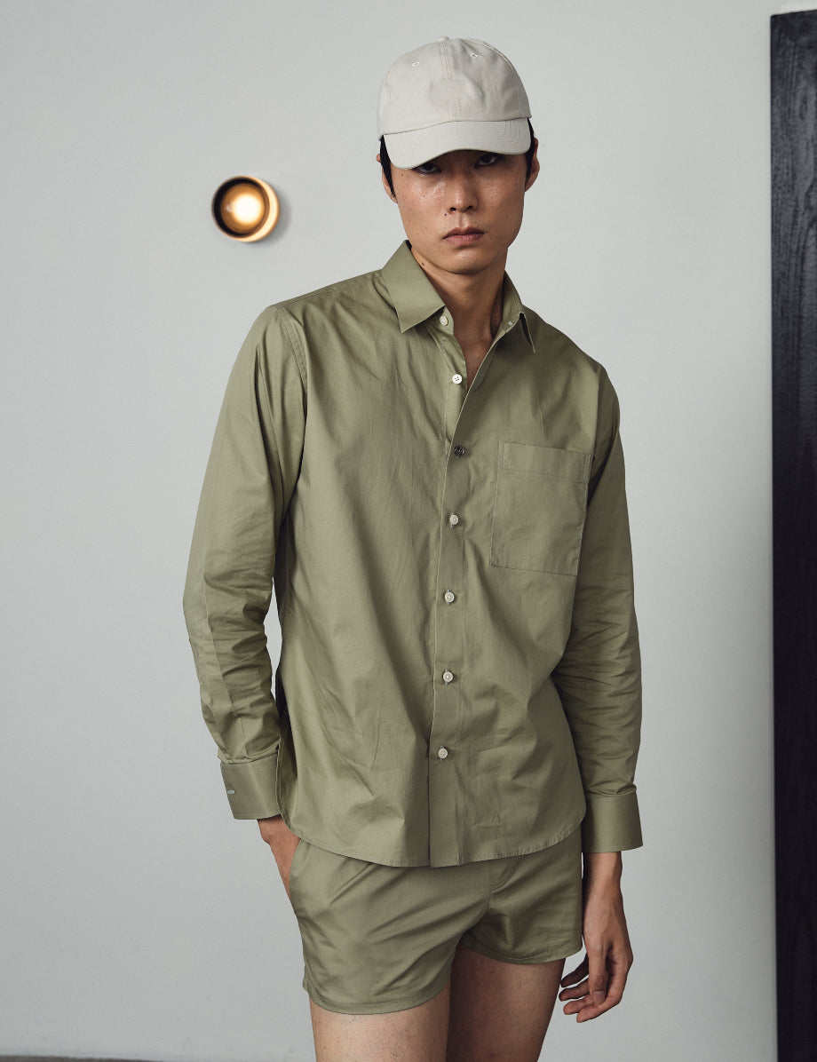 Person wearing a green shirt and shorts with a beige cap against a plain background