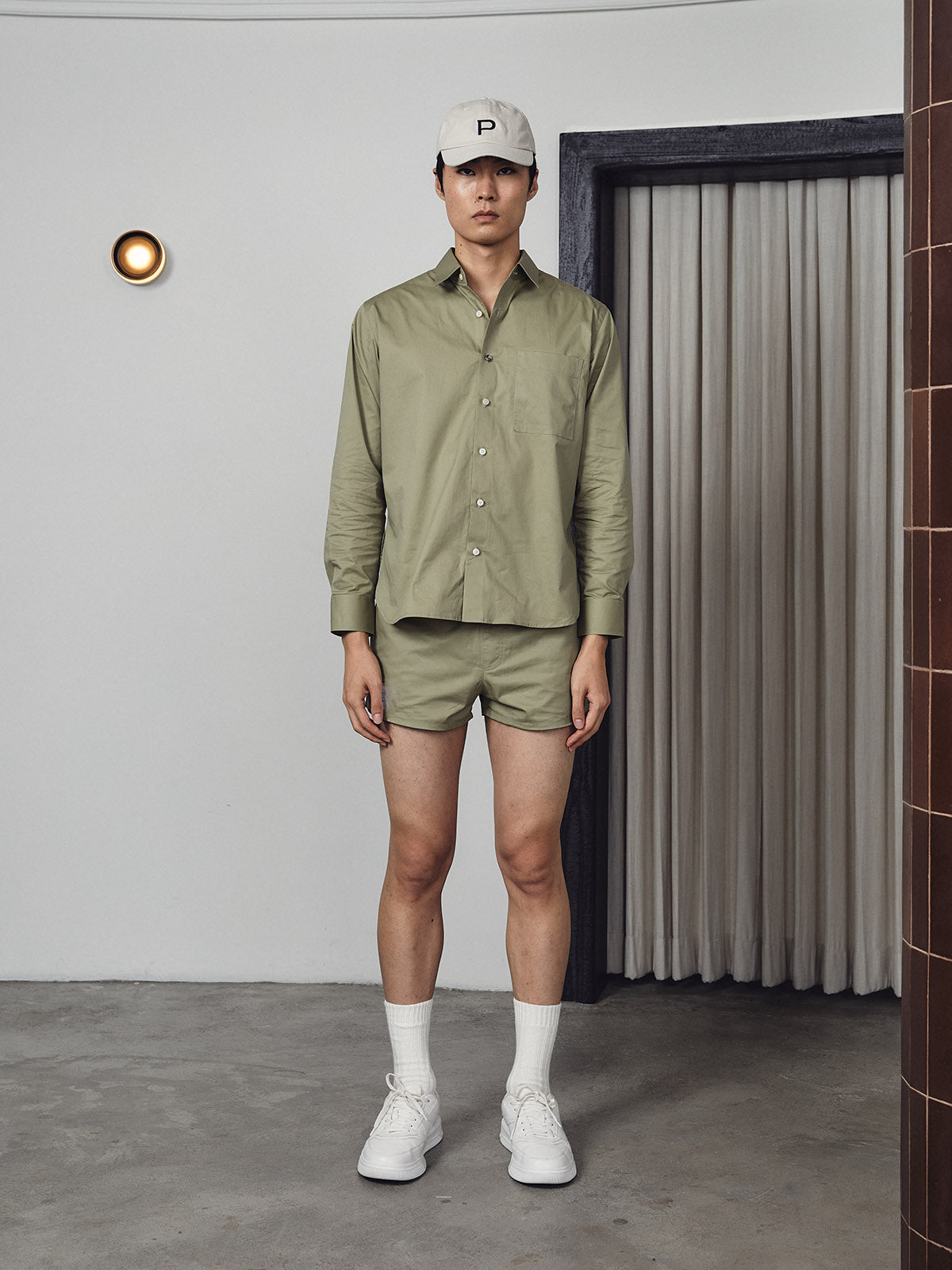 Person wearing a green shirt and shorts with a white cap indoors.