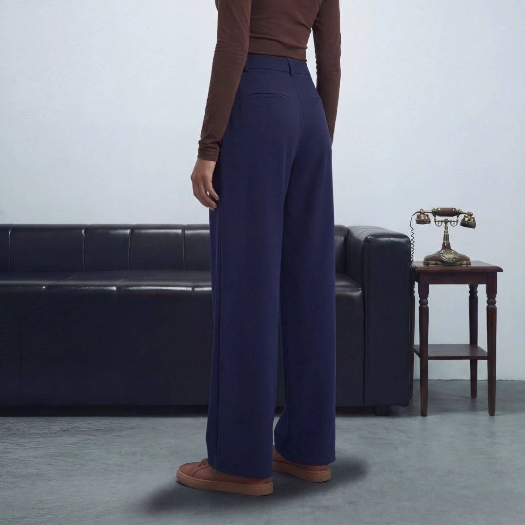 Person wearing blue pants and brown shoes standing in a room with a black leather couch and wooden table.