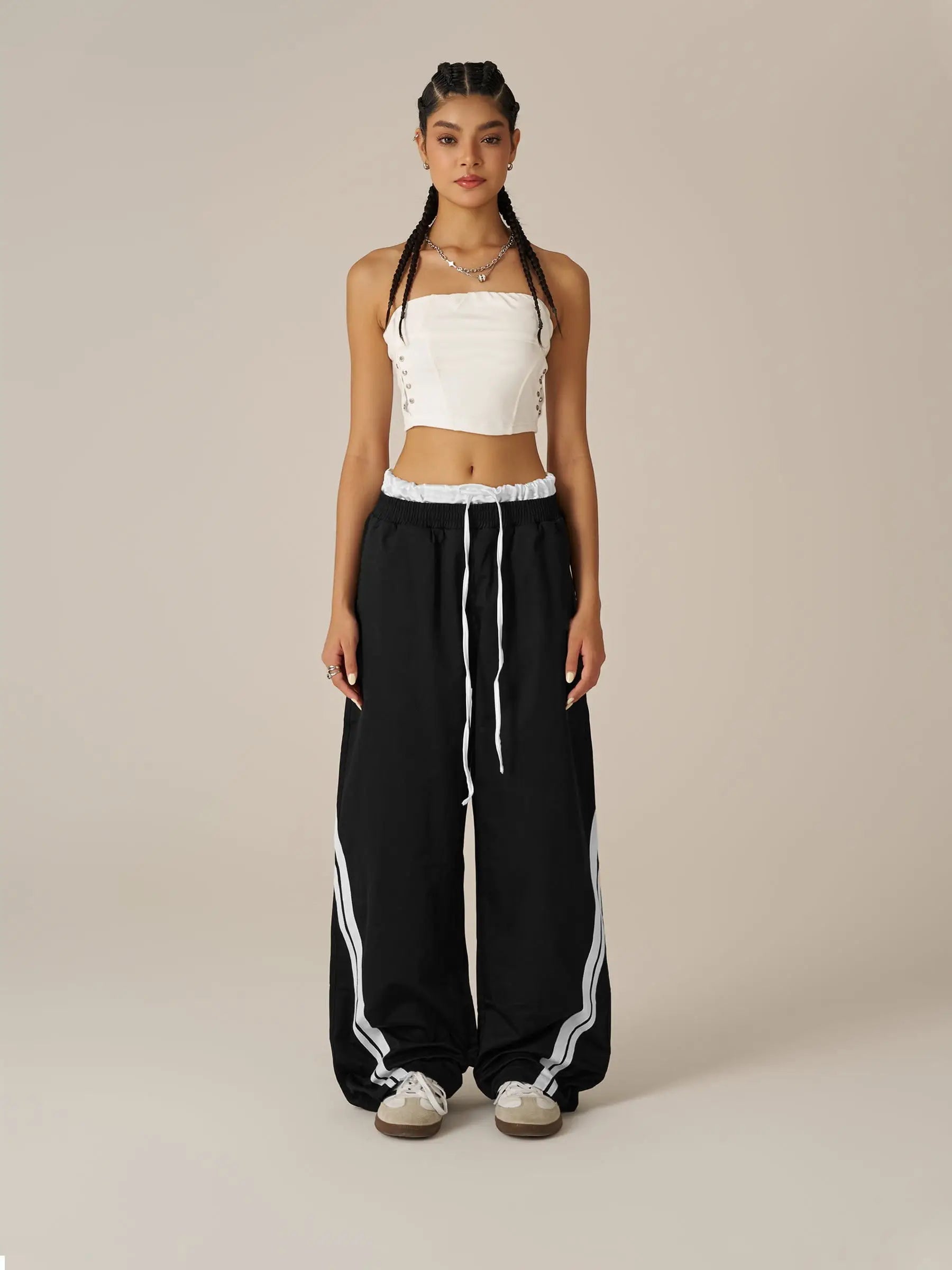 Woman wearing a white crop top and black pants with white stripes on a beige background