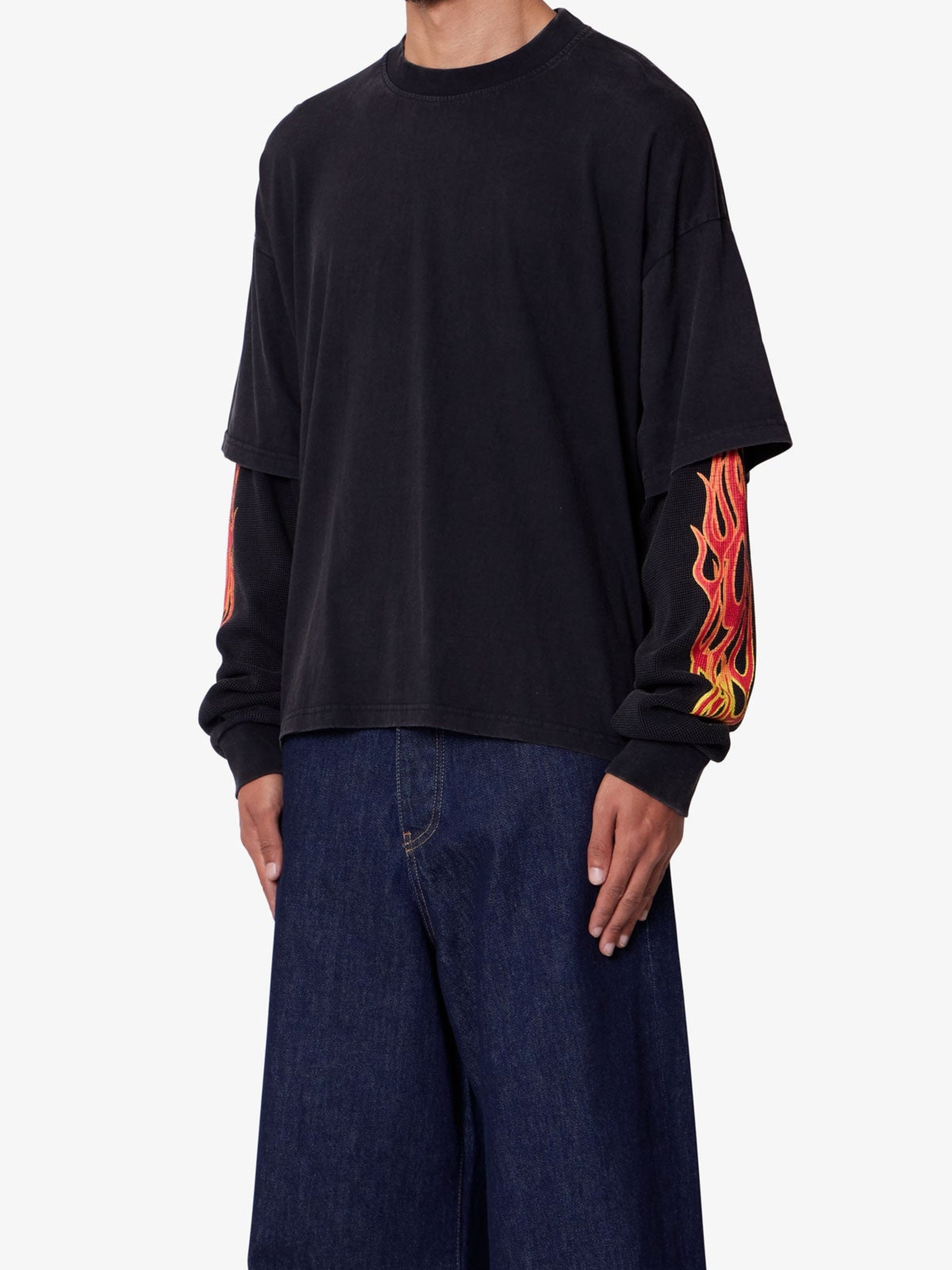 Person wearing a black long-sleeve shirt with flame designs on sleeves against a white background