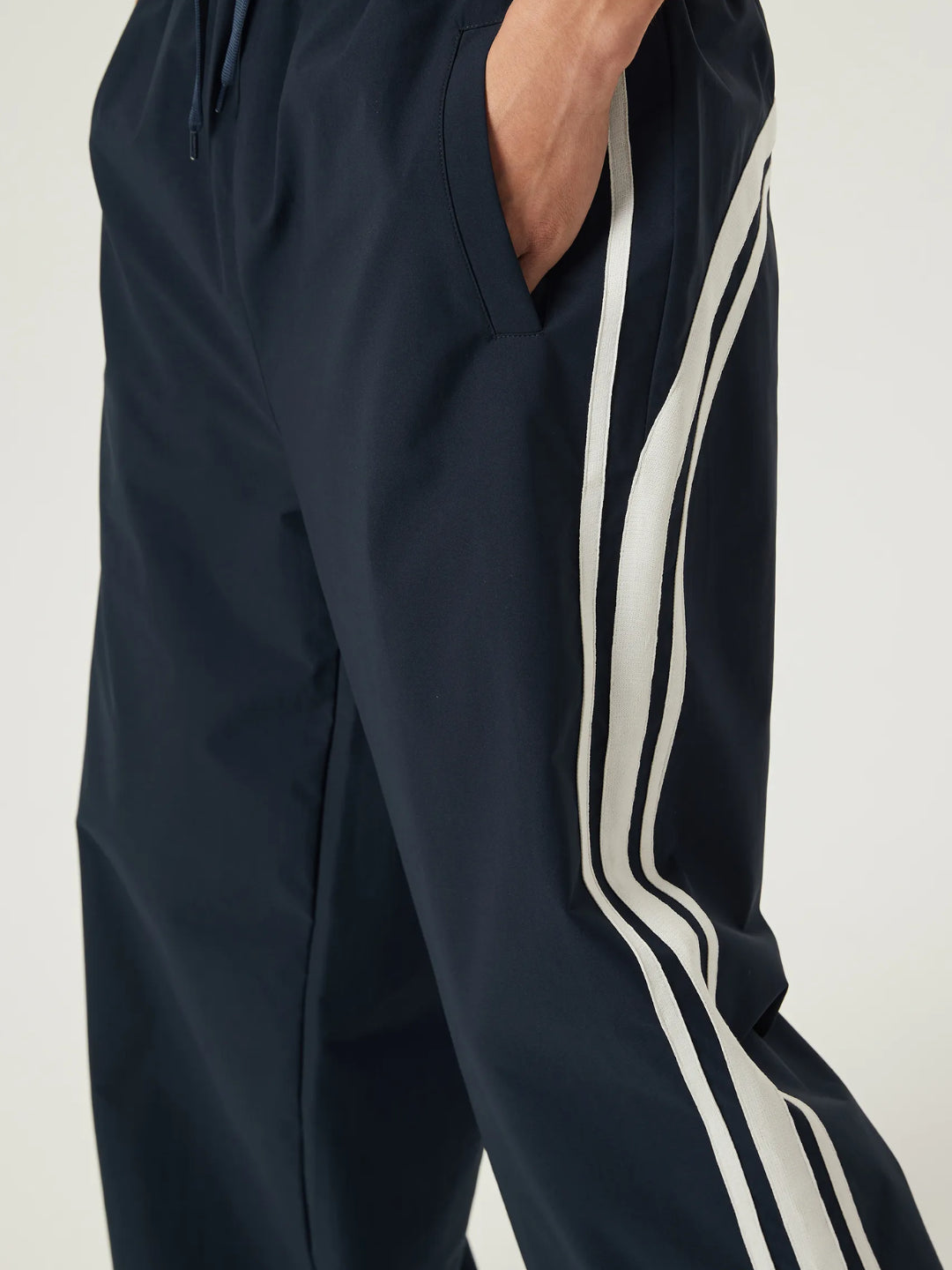navy blue race track pants with white stripes on the side and an elasticated waistband with a drawstring