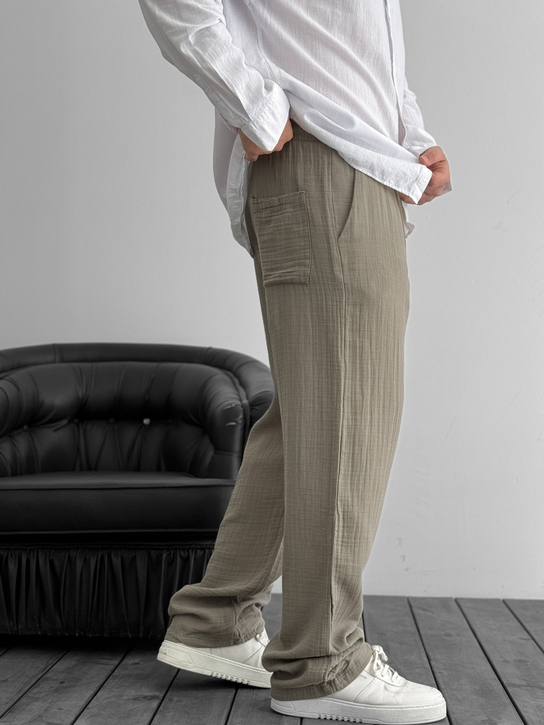 A person standing against a white background, wearing wide-leg gray gauze pants and a white shirt with the sleeves rolled up to the elbows.