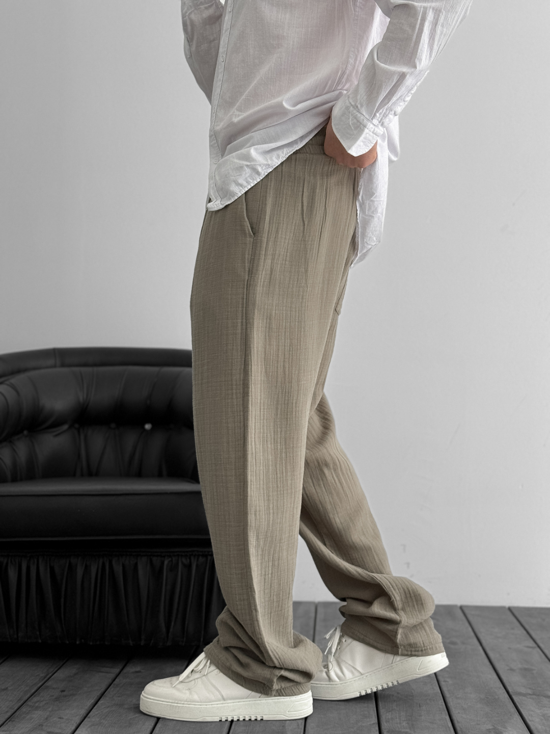 A person standing against a white background, wearing wide-leg gray gauze pants and a white shirt with the sleeves rolled up to the elbows.