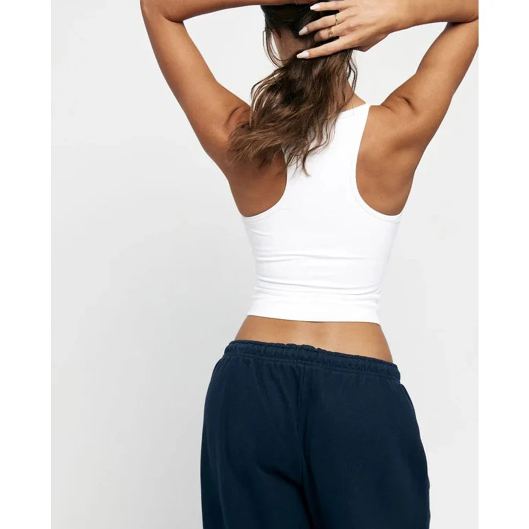 Person wearing a white tank top and navy sweatpants on a light gray background