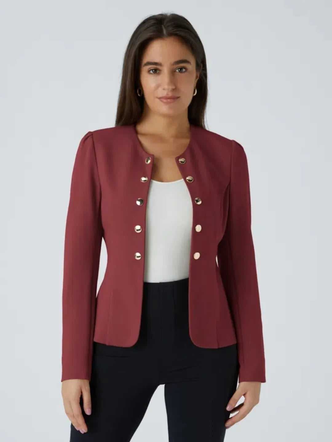 Woman wearing a marooon buisness jacket with gold buttons on a light gray background
