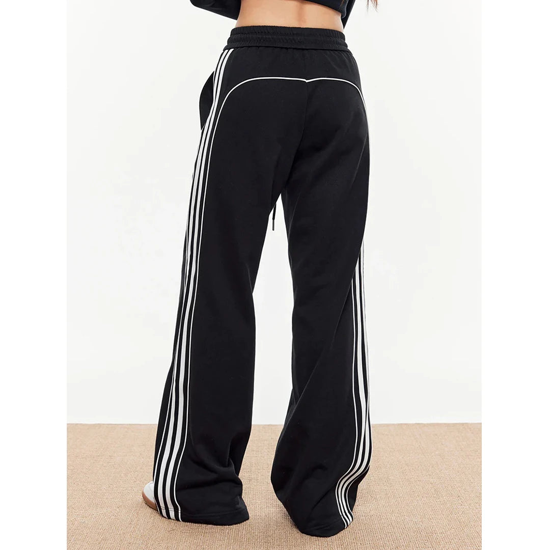 Black sweatpants with white stripes on a beige floor.