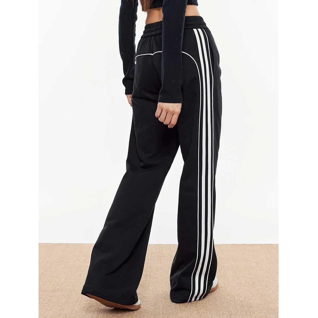 Black track pants with white stripes worn by a person on a beige carpet.
