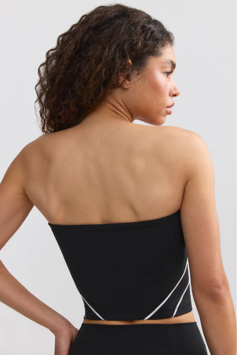 A woman sitting on the floor wearing a black bandeau top and black pants, holding a soccer ball.