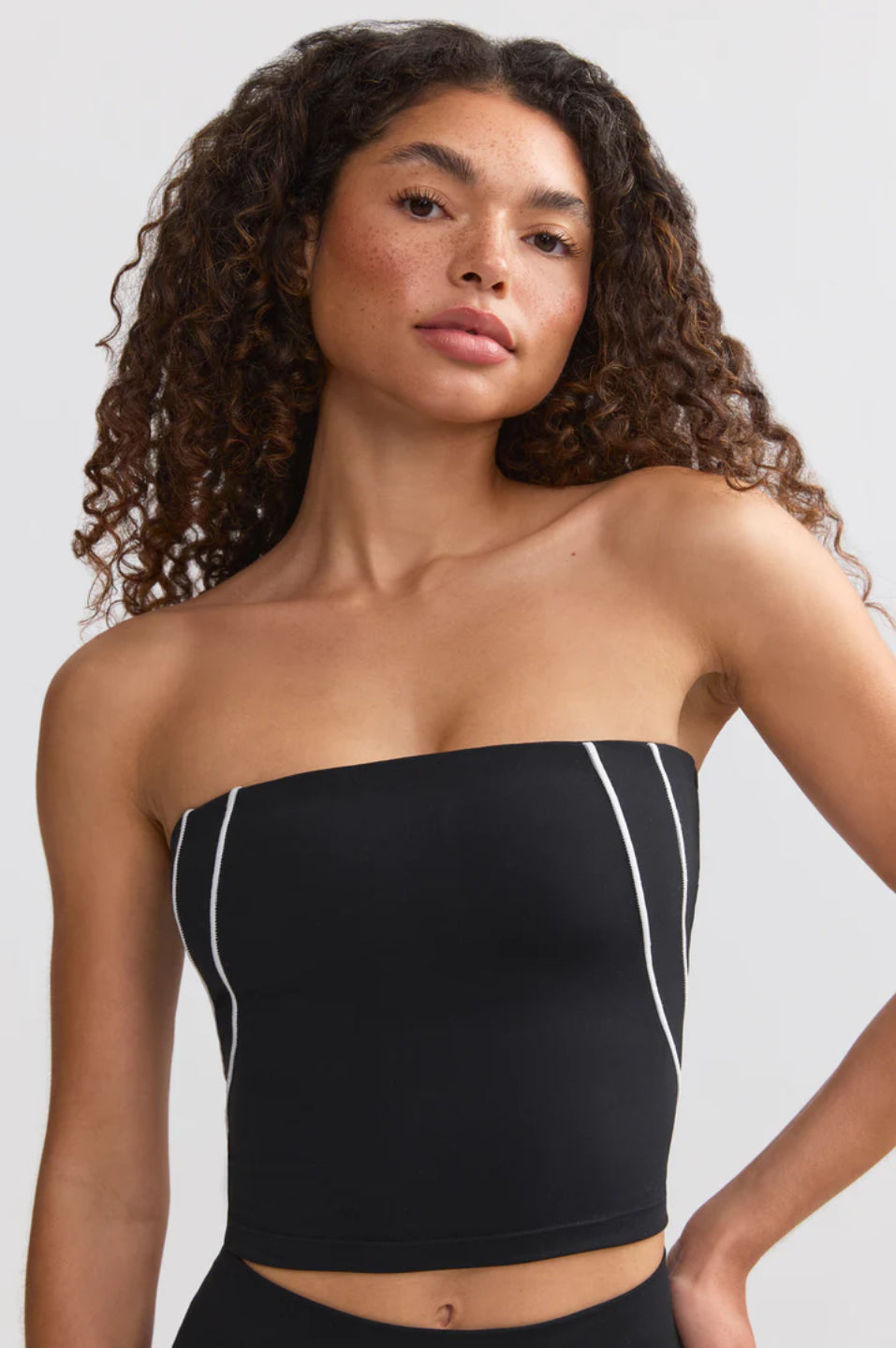 A woman sitting on the floor wearing a black bandeau top and black pants, holding a soccer ball.