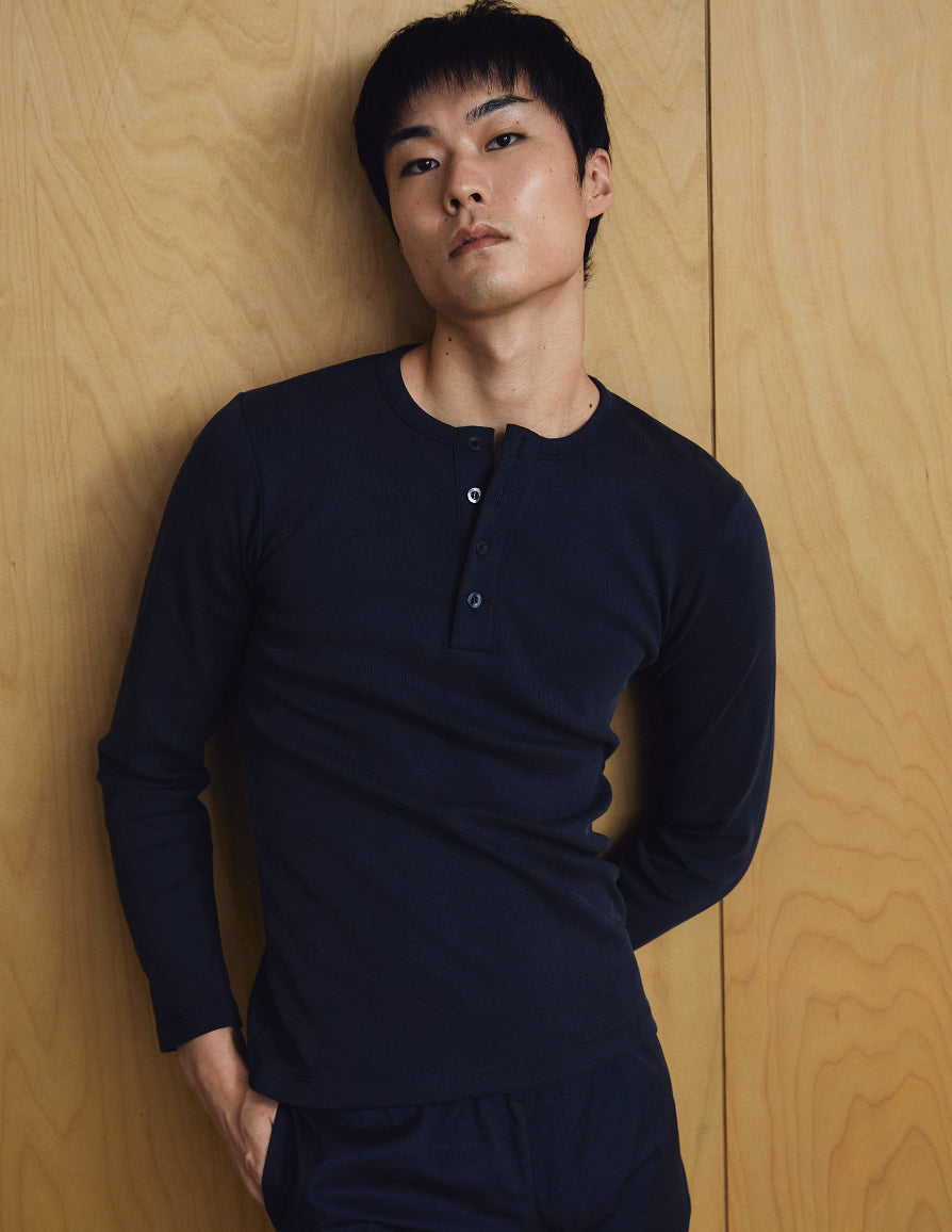 Man wearing a dark blue long-sleeve shirt against a wooden panel background