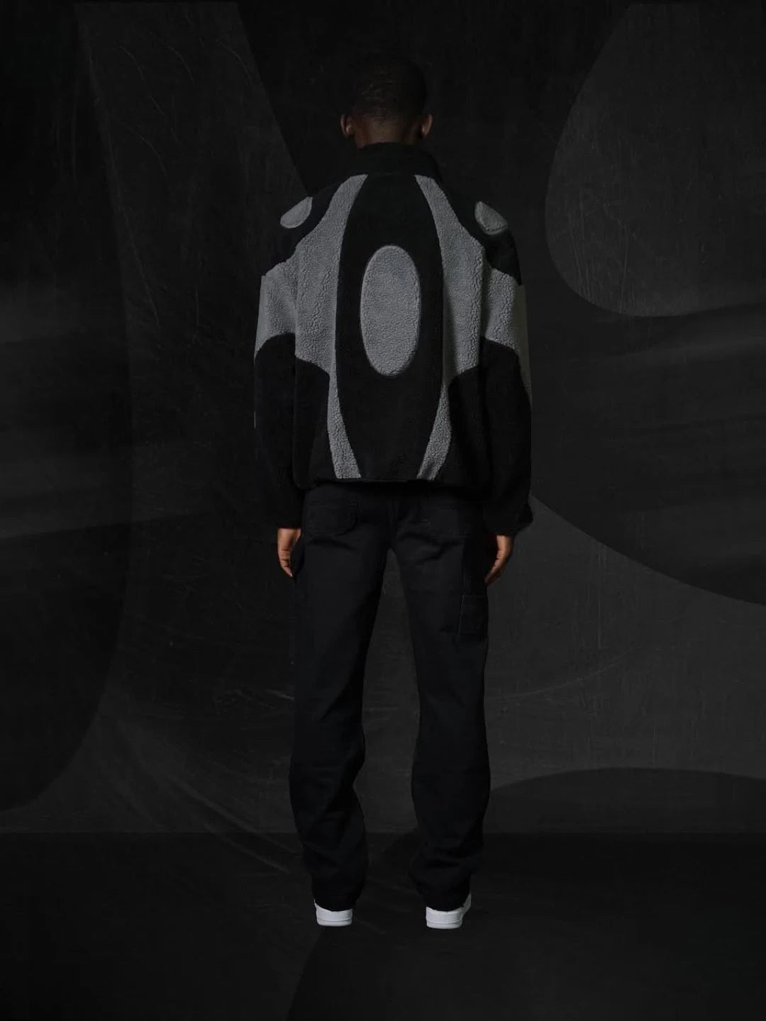 Person wearing a black and gray jacket with back against a dark background