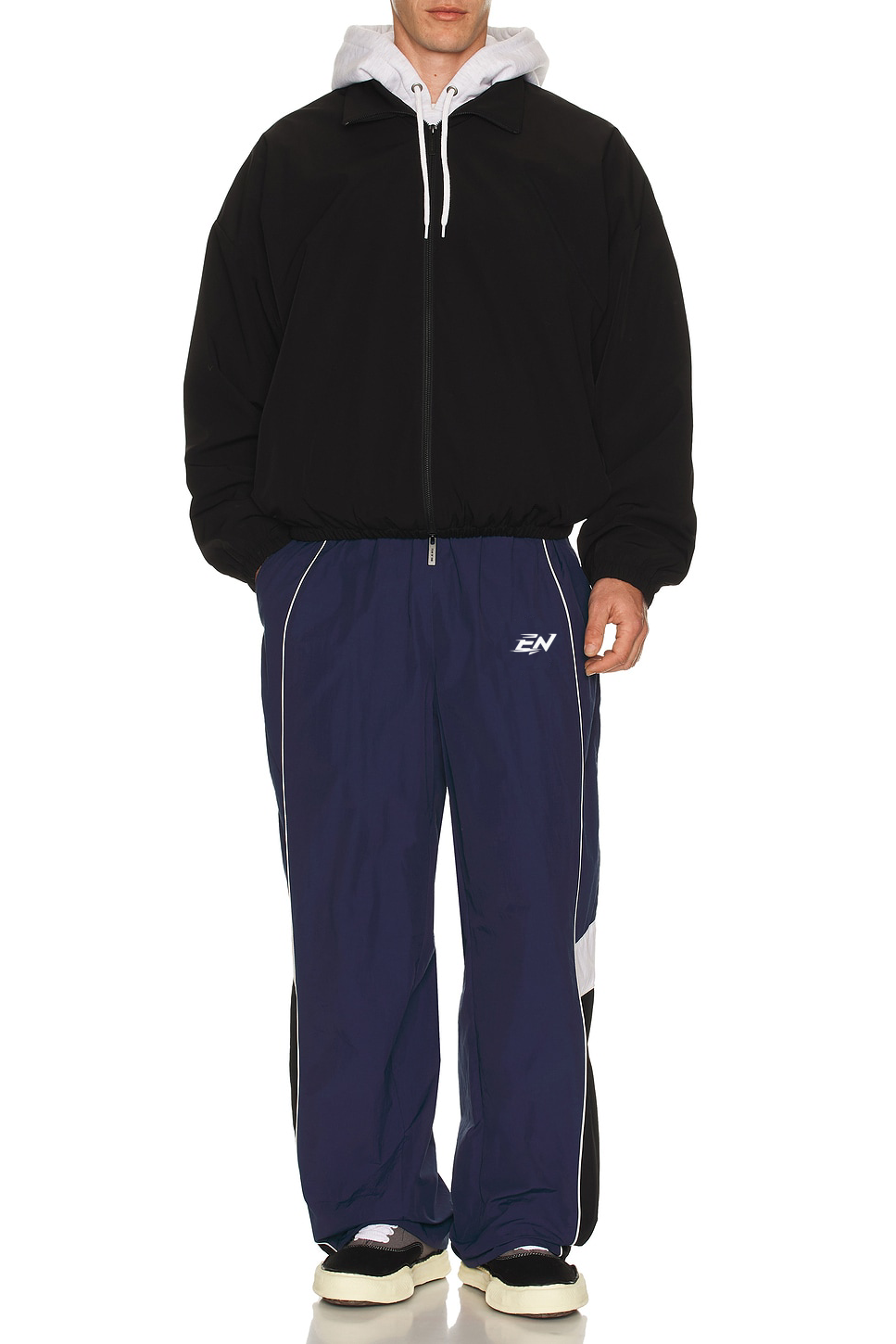Person wearing a black hoodie and navy tracksuit with a logo on a white background